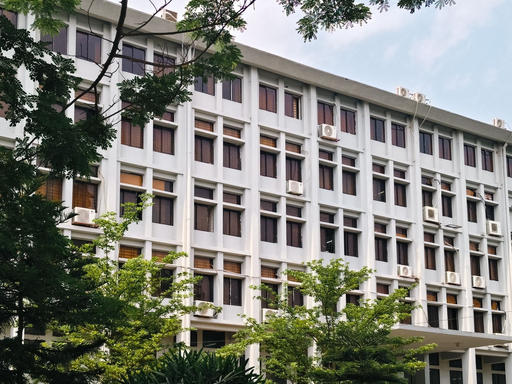 Modern office building exterior with air conditioners and lush green trees
